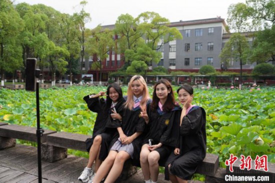 6月19日,时值一年毕业季,四川大学望江校区荷花池里的荷花盛开,成为了毕业生们的打卡圣地,吸引了众多毕业生拍照留念。图为毕业生在荷花池边拍照留念。中新社记者 安源 摄